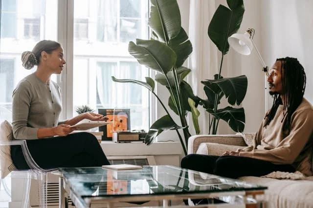 A therapist taking notes while talking with a client on a sofa